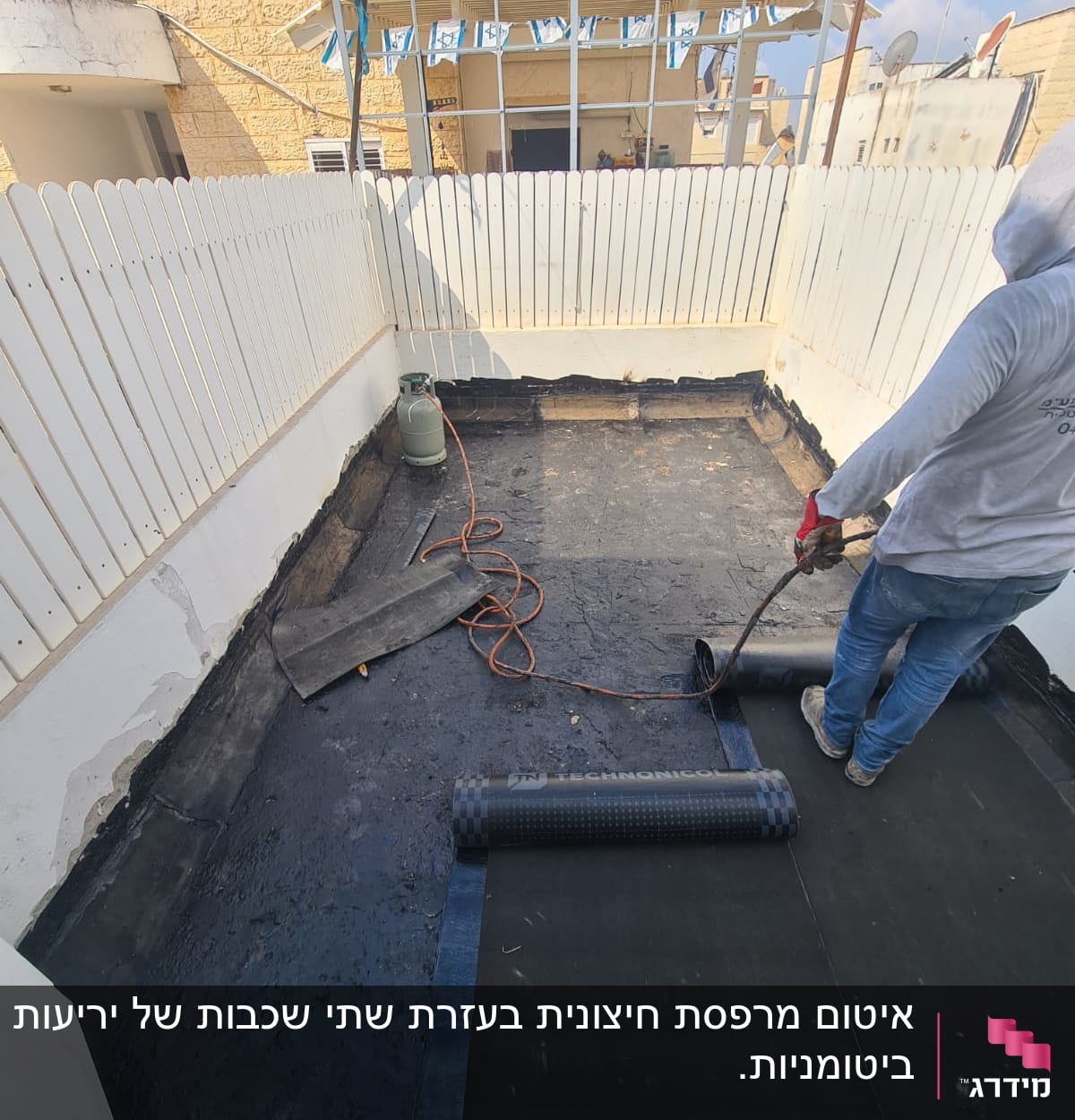 אדם מיישם יריעות איטום על גג בעזרת מבער גז